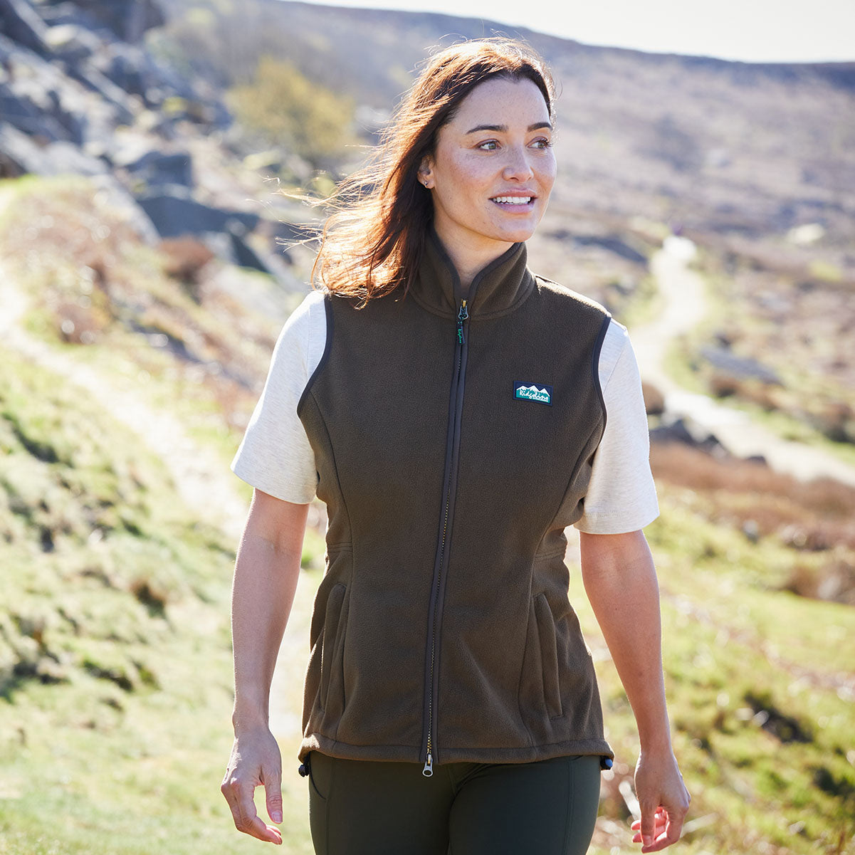 Woman wearing a brown vest with a Ridgeline Clothing logo in a natural setting