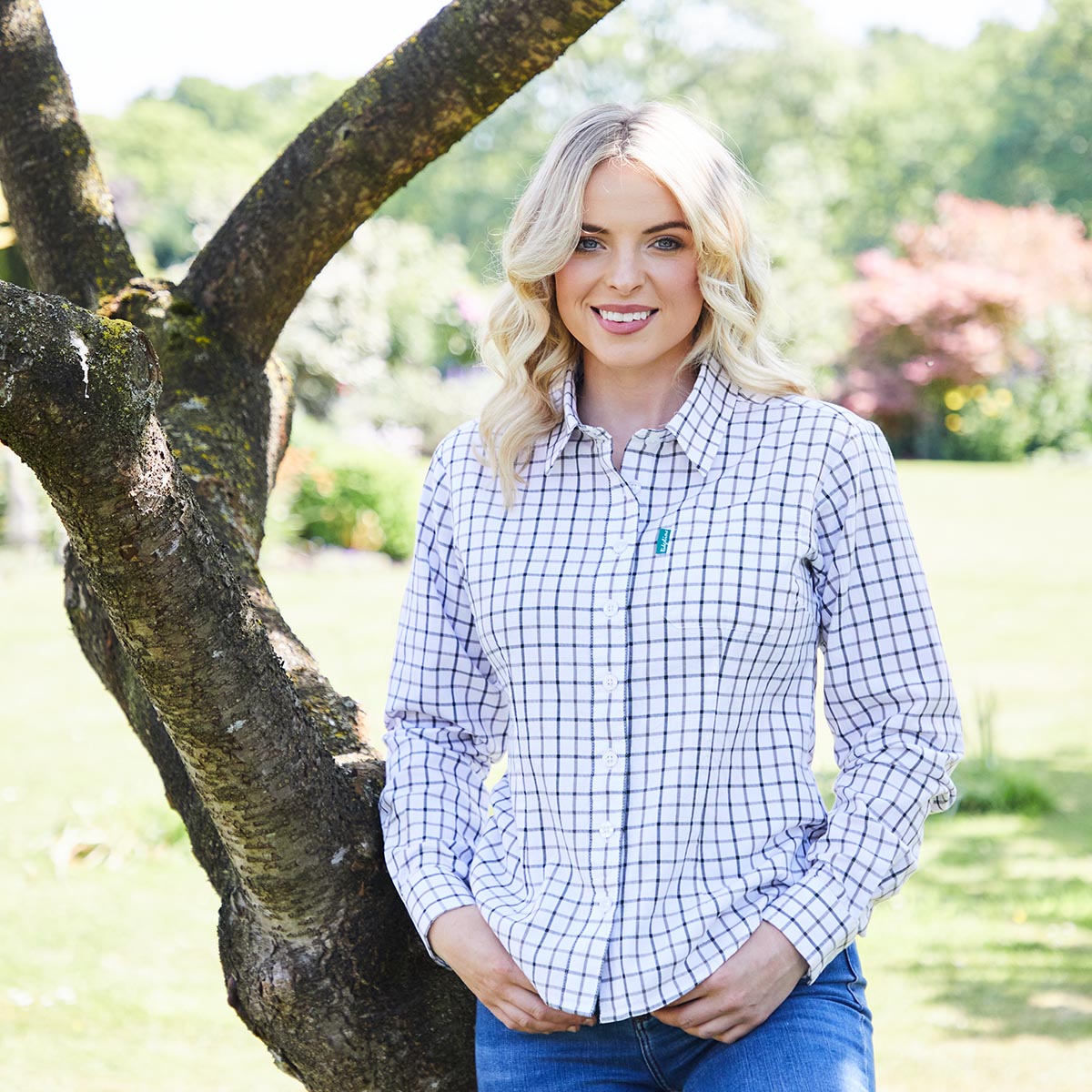 Woman wearing a blue and white checkered shirt standing outdoors near a tree