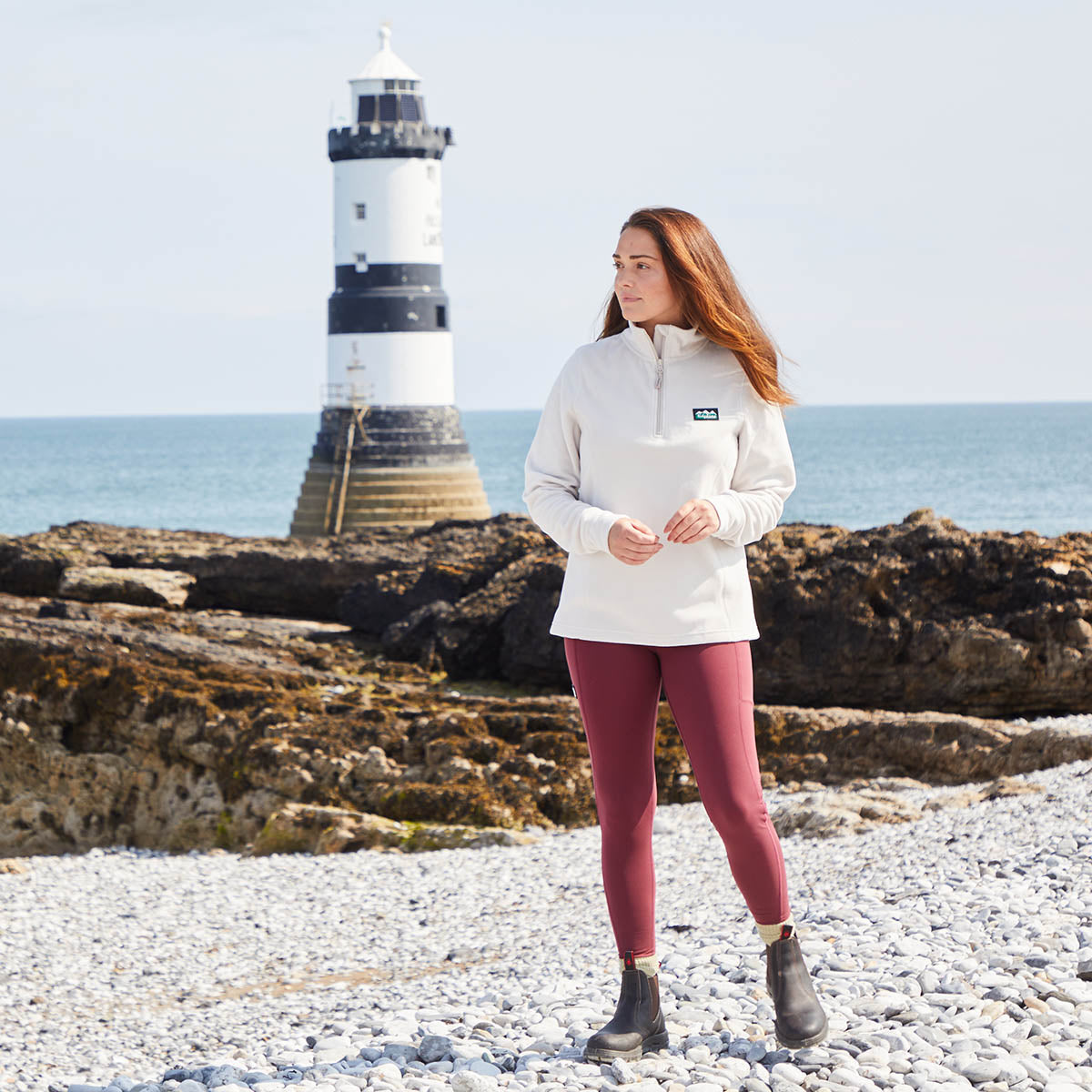 Woman standing on a rocky beach with a lighthouse in the background