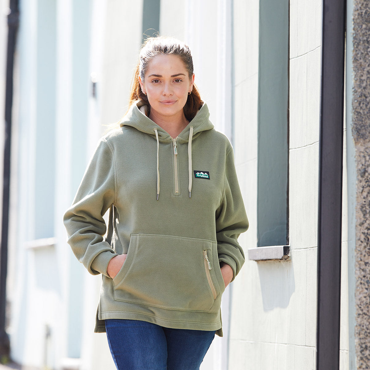 Woman wearing a green hoodie with a Ridgeline Clothing logo on chest, standing outdoors.