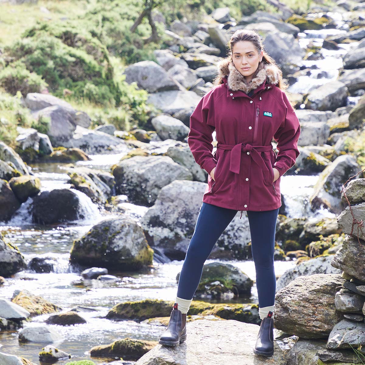 Woman in a red jacket standing by a rocky stream