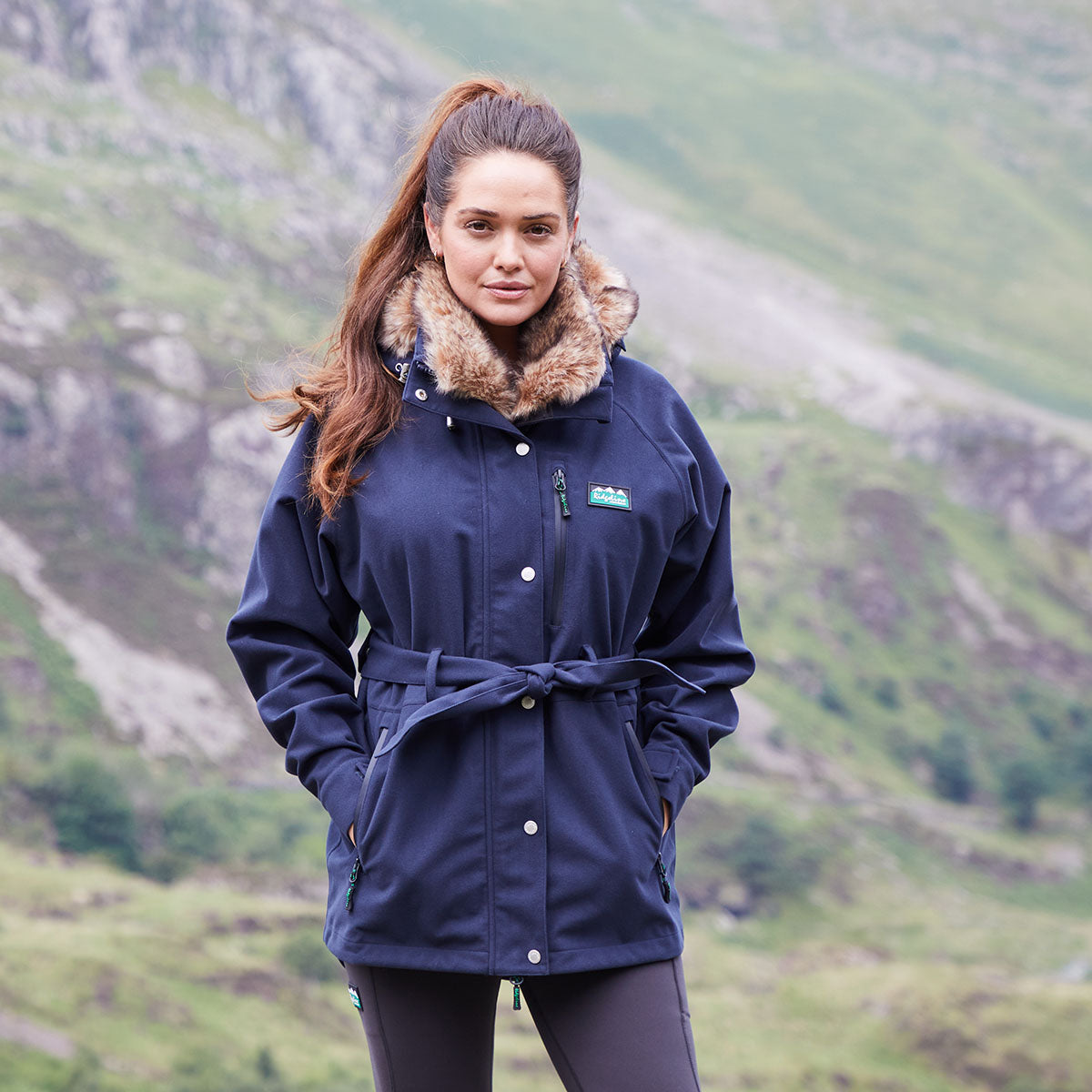 Woman wearing a navy blue coat with fur collar in a mountainous landscape