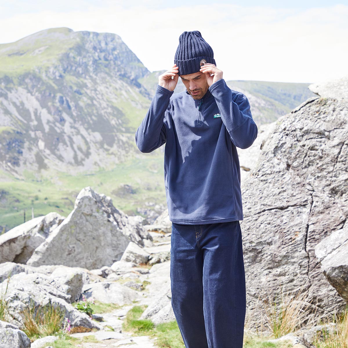 Person wearing a blue Fleece with a Ridgeline logo on chest, standing in a mountainous landscape.