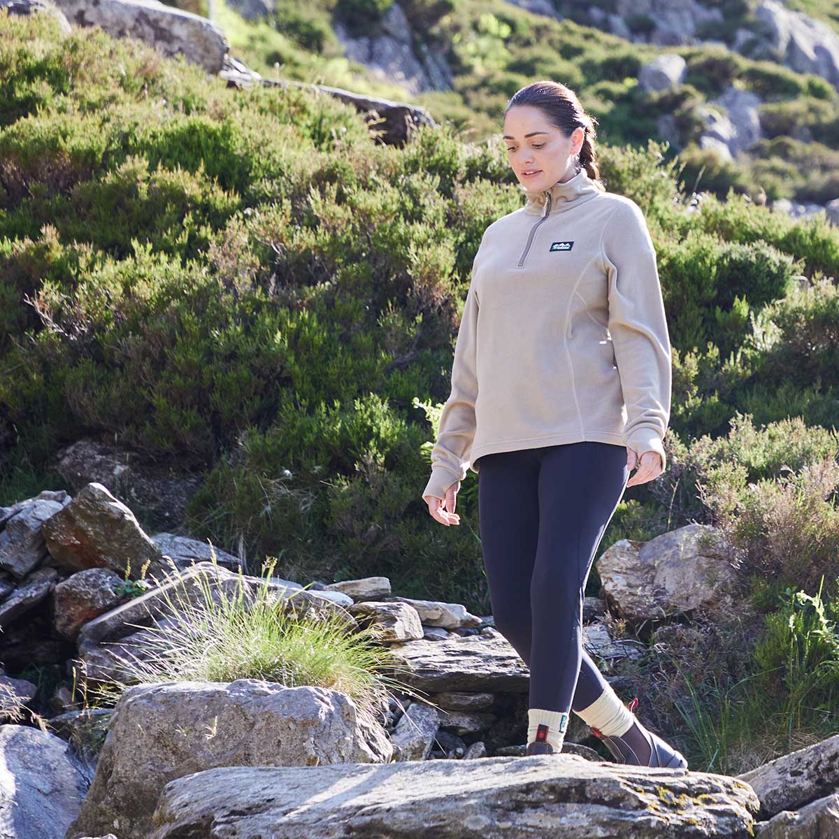 Woman walking on a rocky trail in a natural setting wearing a cream fleece with Ridgeline Clothing Logo