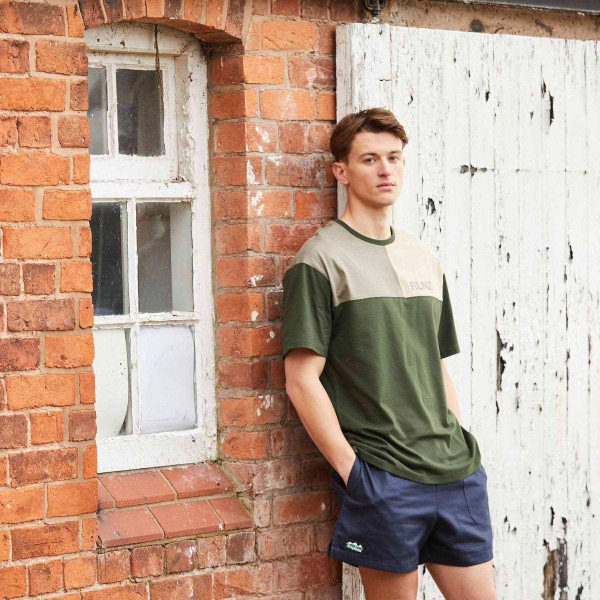 Person wearing a green and beige shirt leaning against a brick wall.