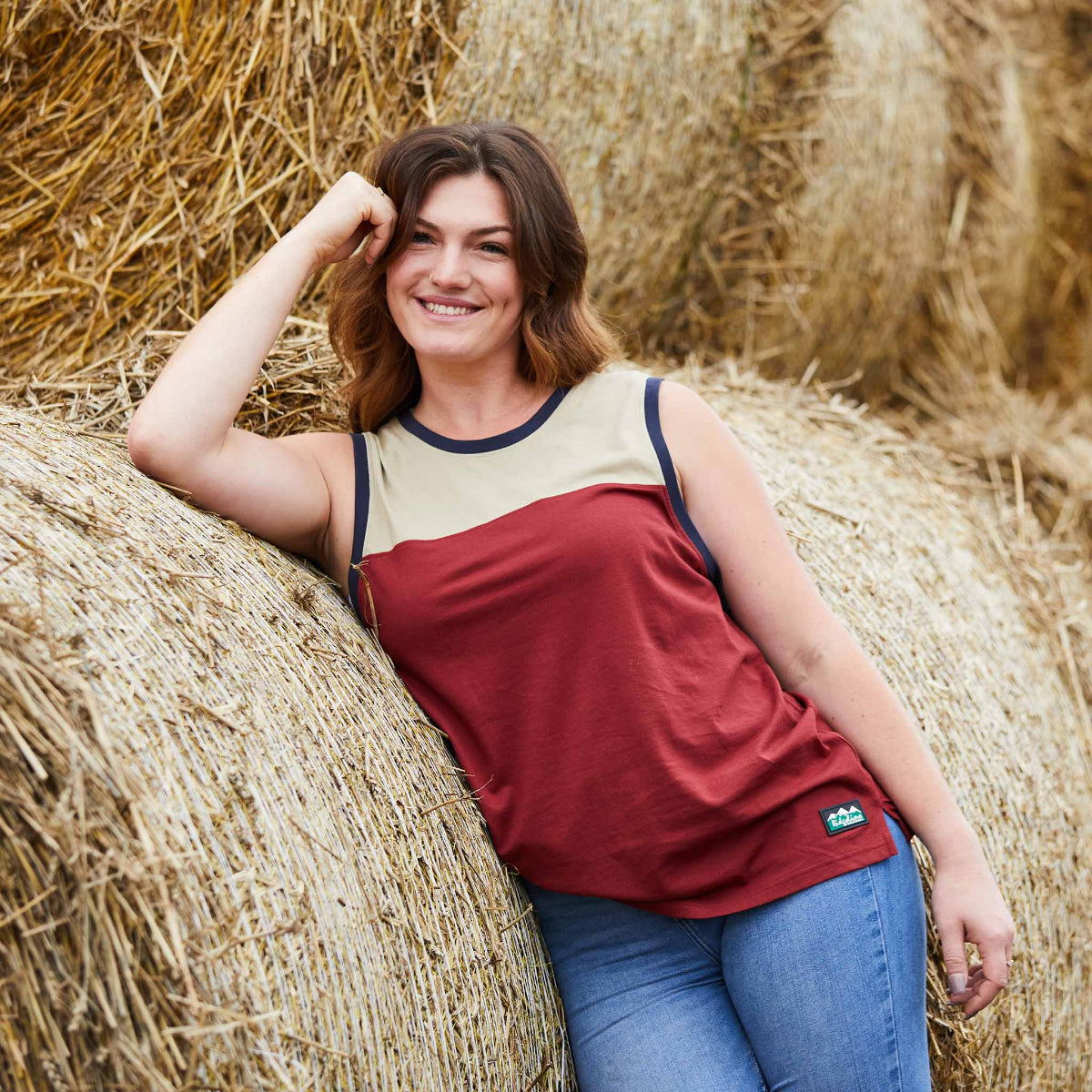 Woman leaning against a hay bale in a field in a Ridgeline vest