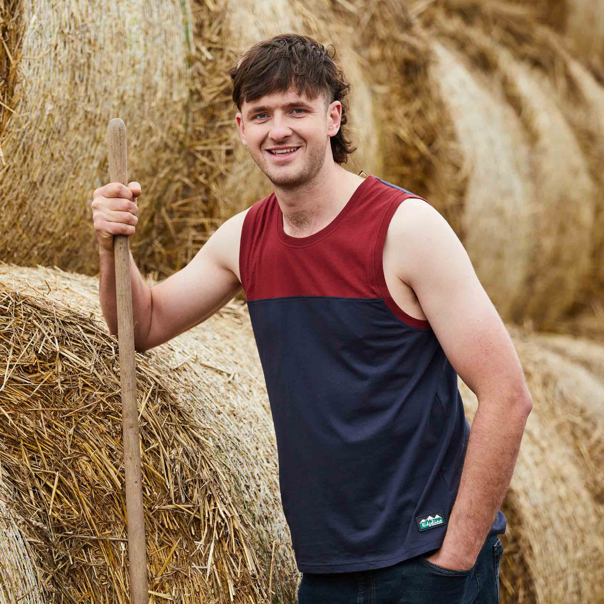 Man holding a stick standing among hay bales