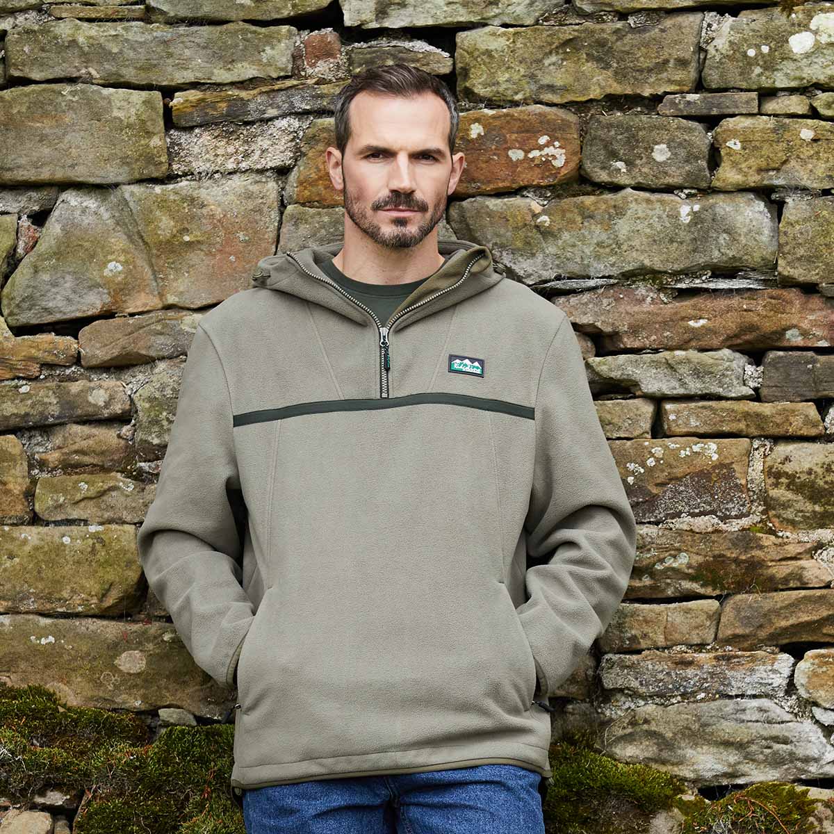 Man wearing a Grey pullover with a Ridgeline Clothing brand logo against a stone wall.