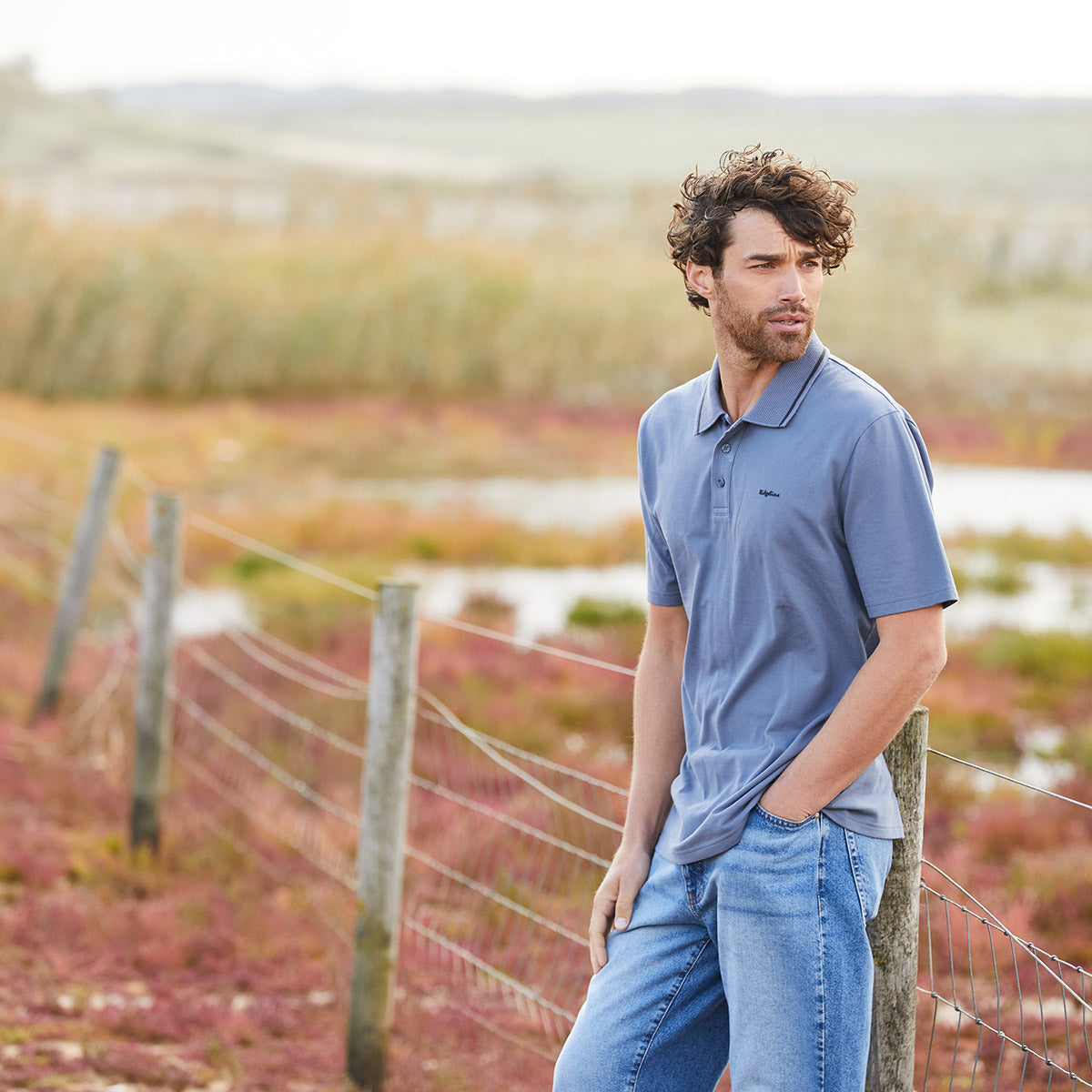 Man wearing a blue polo shirt leaning on fence
