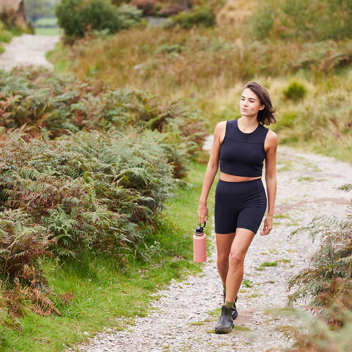 Woman wearing a black sleeveless top and shorts walking through a pathway
