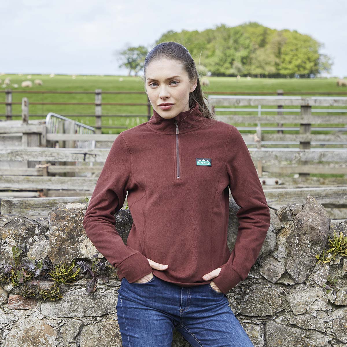 Burgundy half zip fleece pullover, outdoor view, worn with blue jeans in a farm lifestyle background.