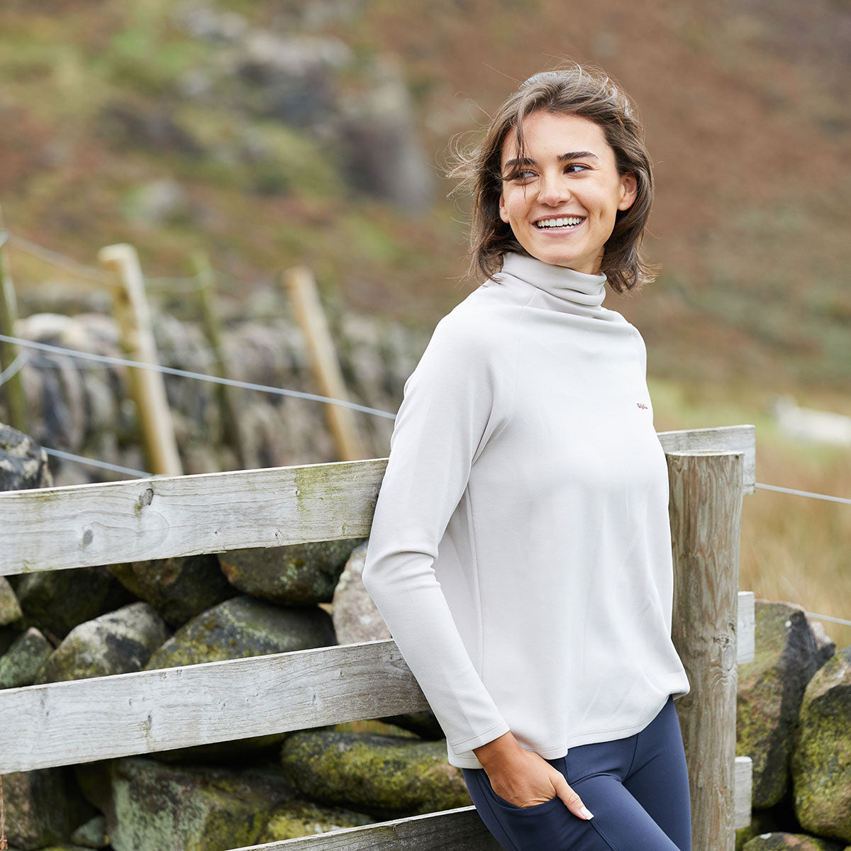 Woman standing by a wooden fence with a scenic background