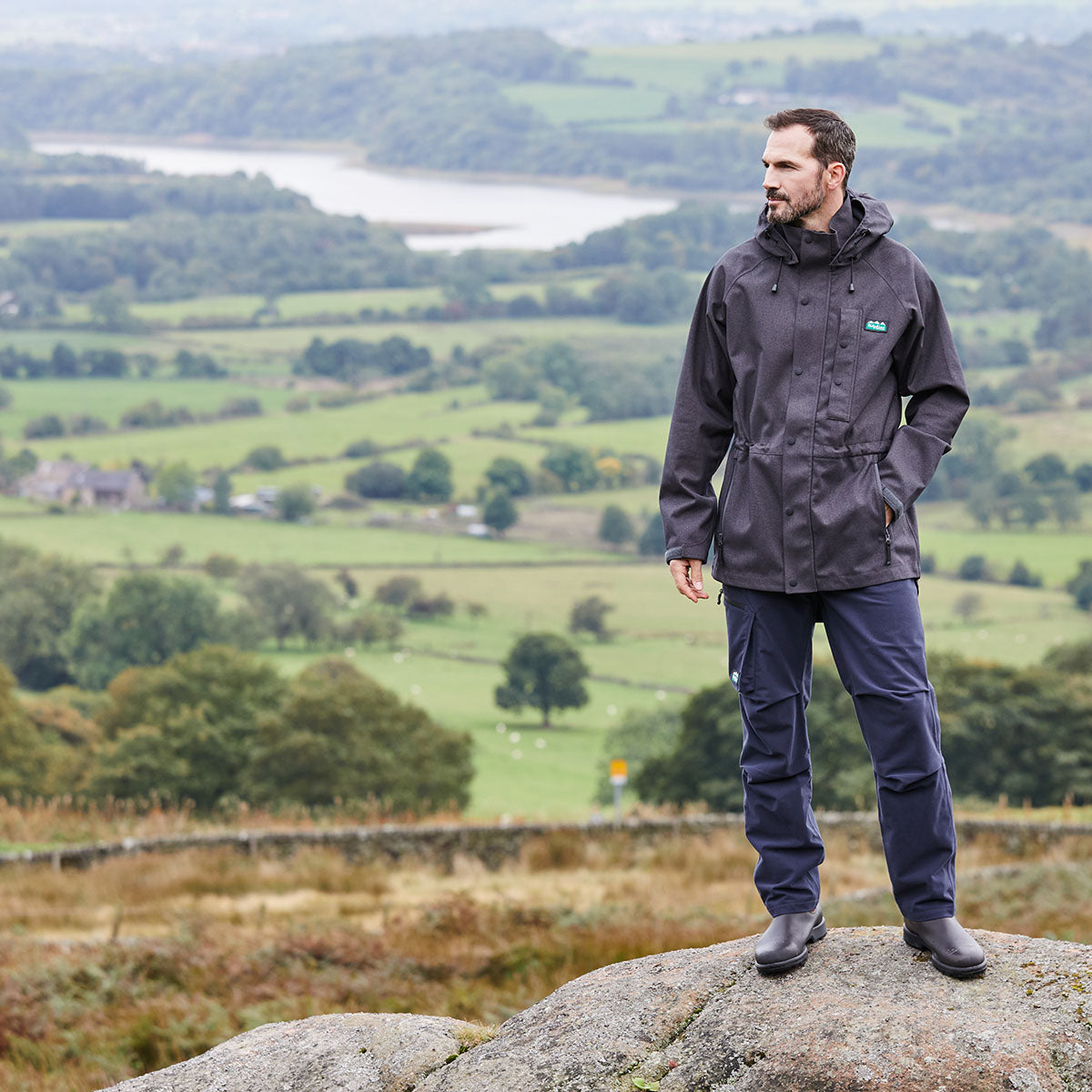Man in a raincoat standing on a rock with a scenic landscape in the background