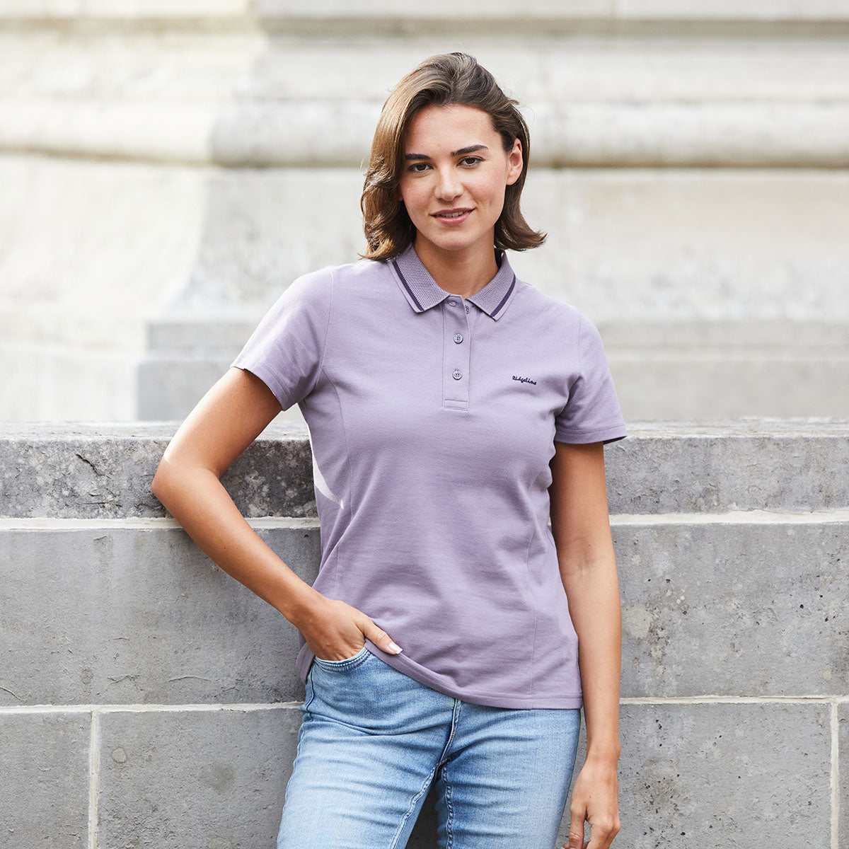 Woman wearing a purple polo shirt leaning on brick wall