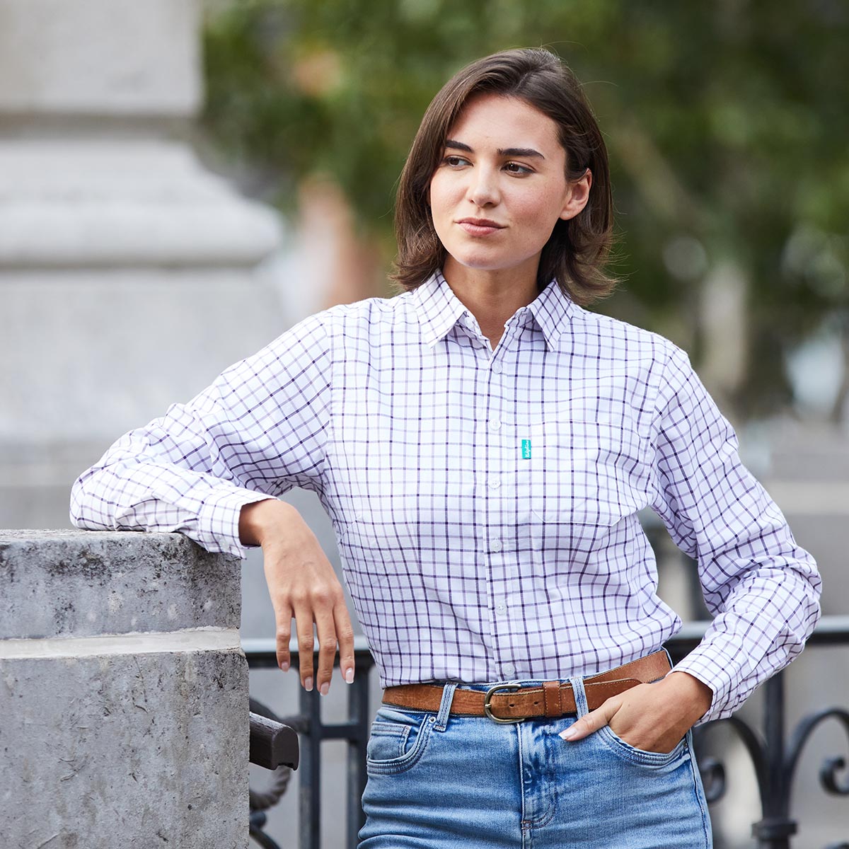 Woman wearing a checkered shirt and jeans standing outdoors.