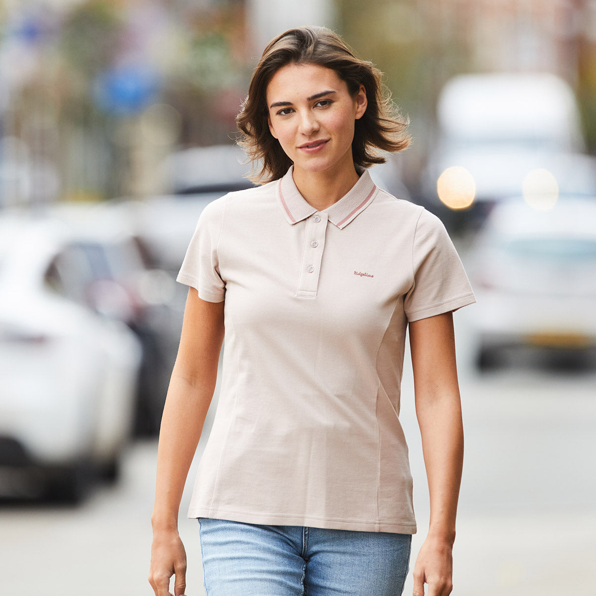 Woman wearing a pink polo shirt walking through city with blurred background