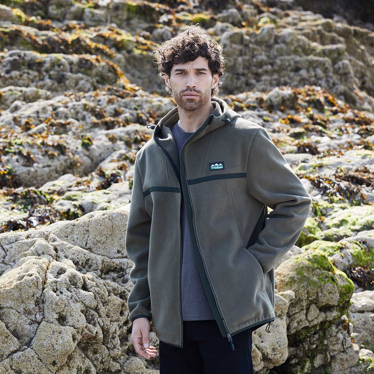 Man wearing a green jacket with a brand logo standing on rocky terrain