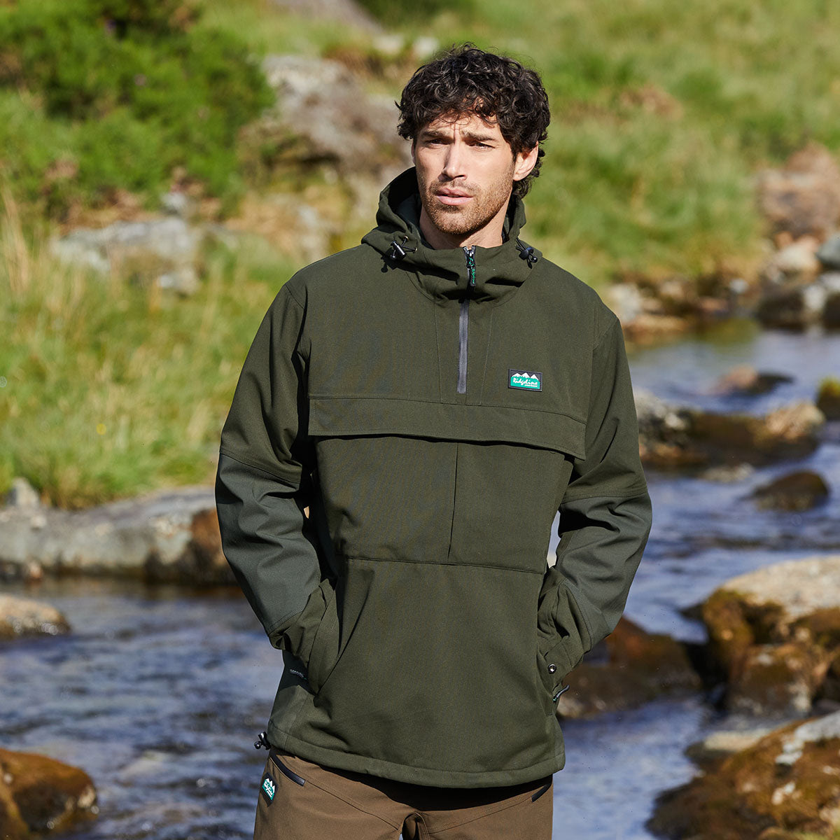 Man wearing a green jacket with a Ridgeline Clothing brand logo standing by a stream.