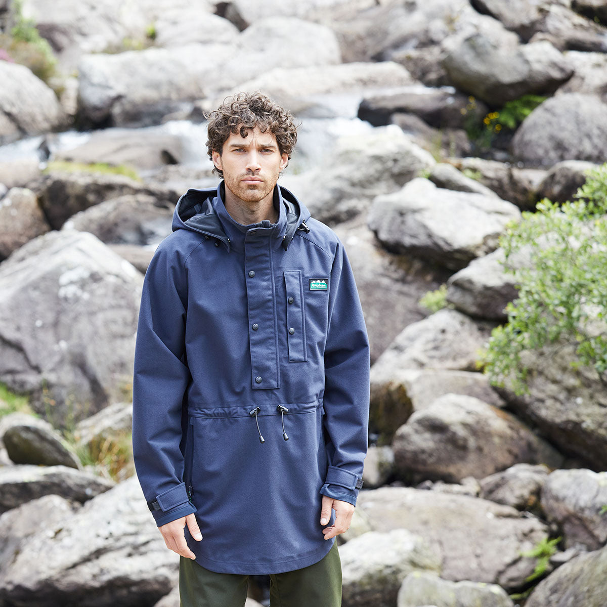 Person wearing a blue waterproof jacket standing in front of rocky terrain