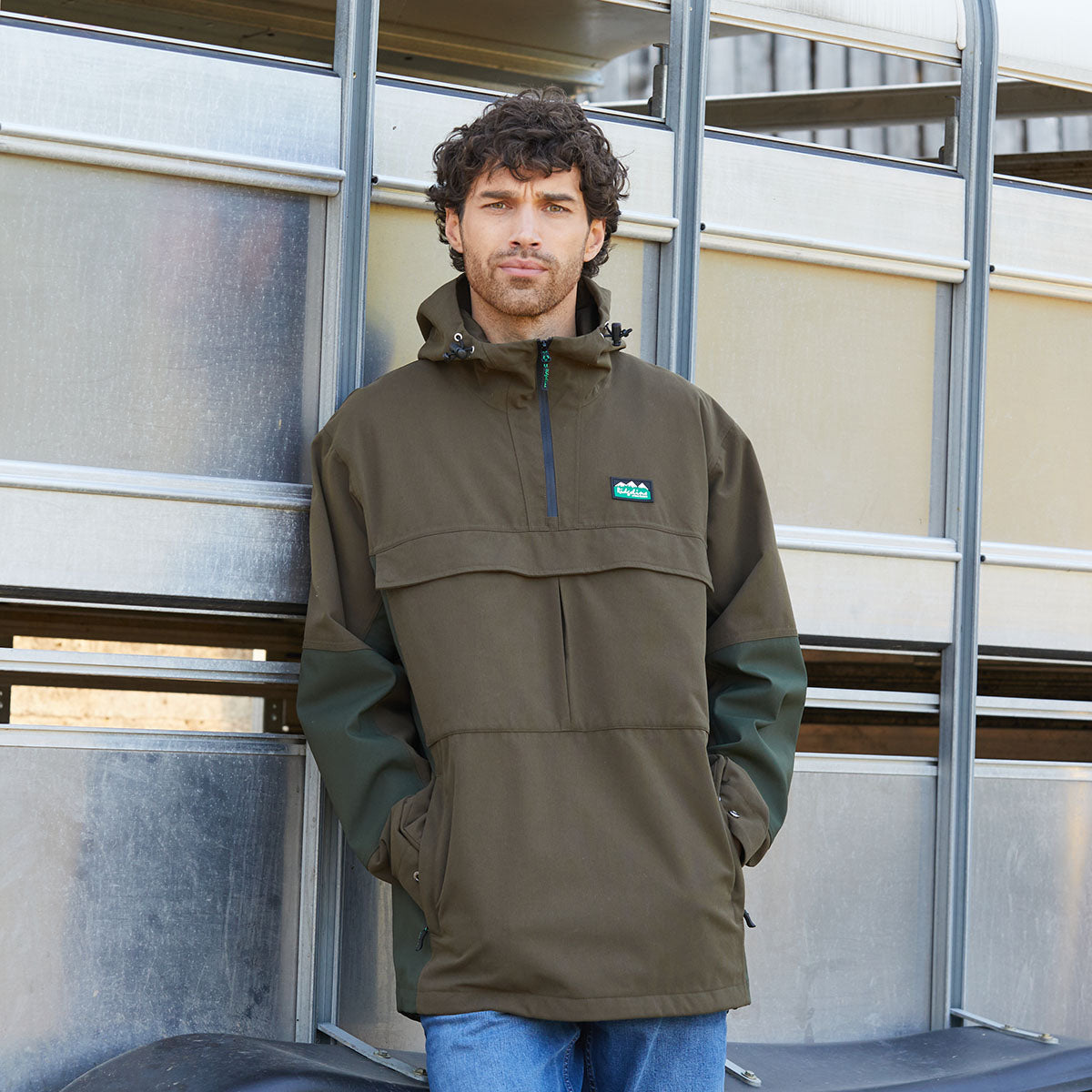 Man wearing a Brown jacket with a Ridgeline Clothing brand logo, standing in front of a metal structure.