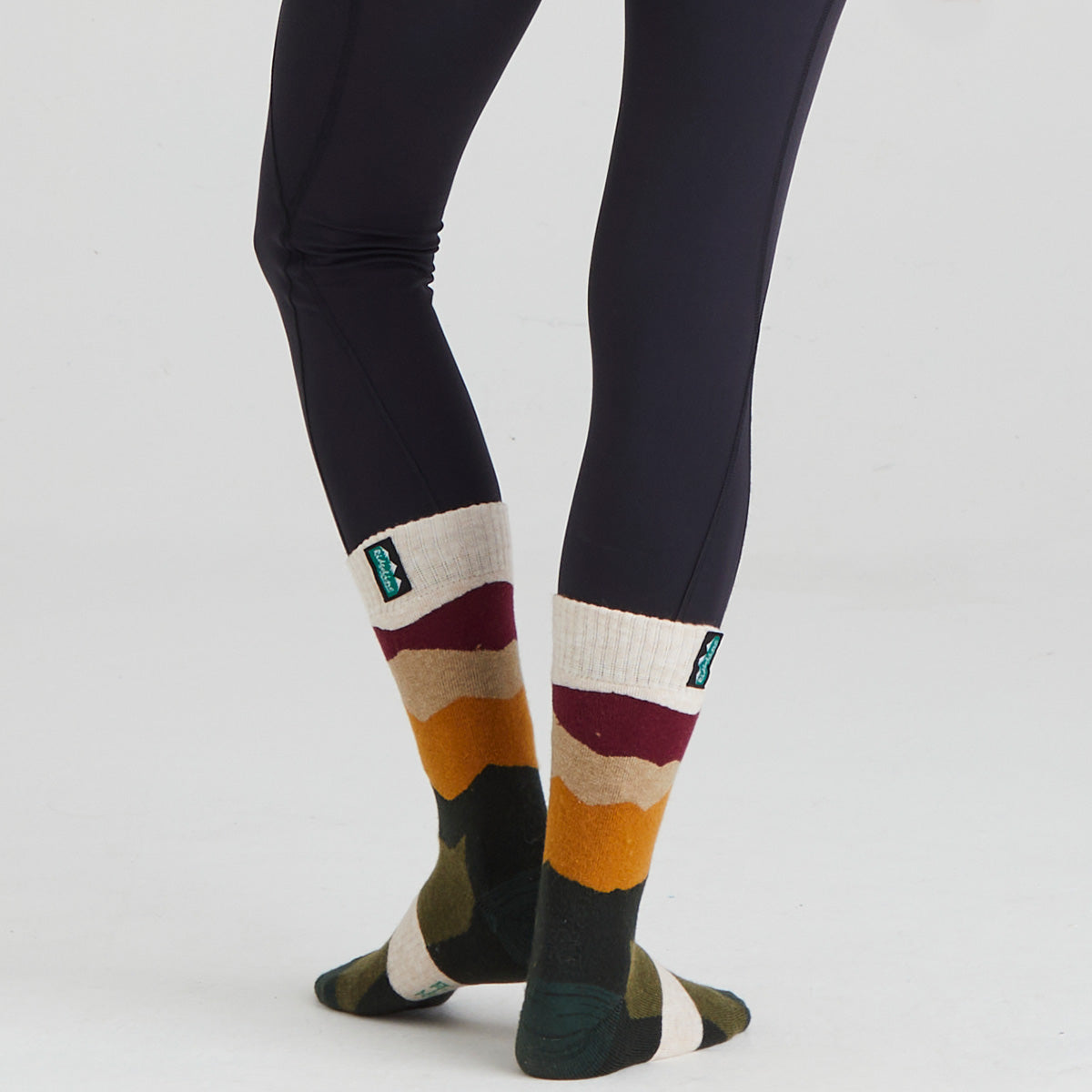 Colourful striped socks with a brand logo worn with dark leggings on a light grey background
