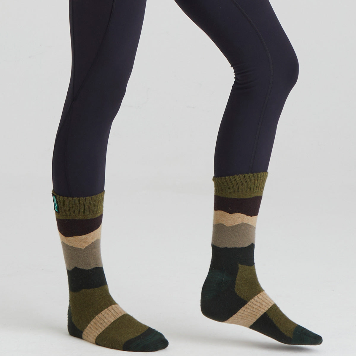 Green and brown striped socks worn with dark leggings on a white background