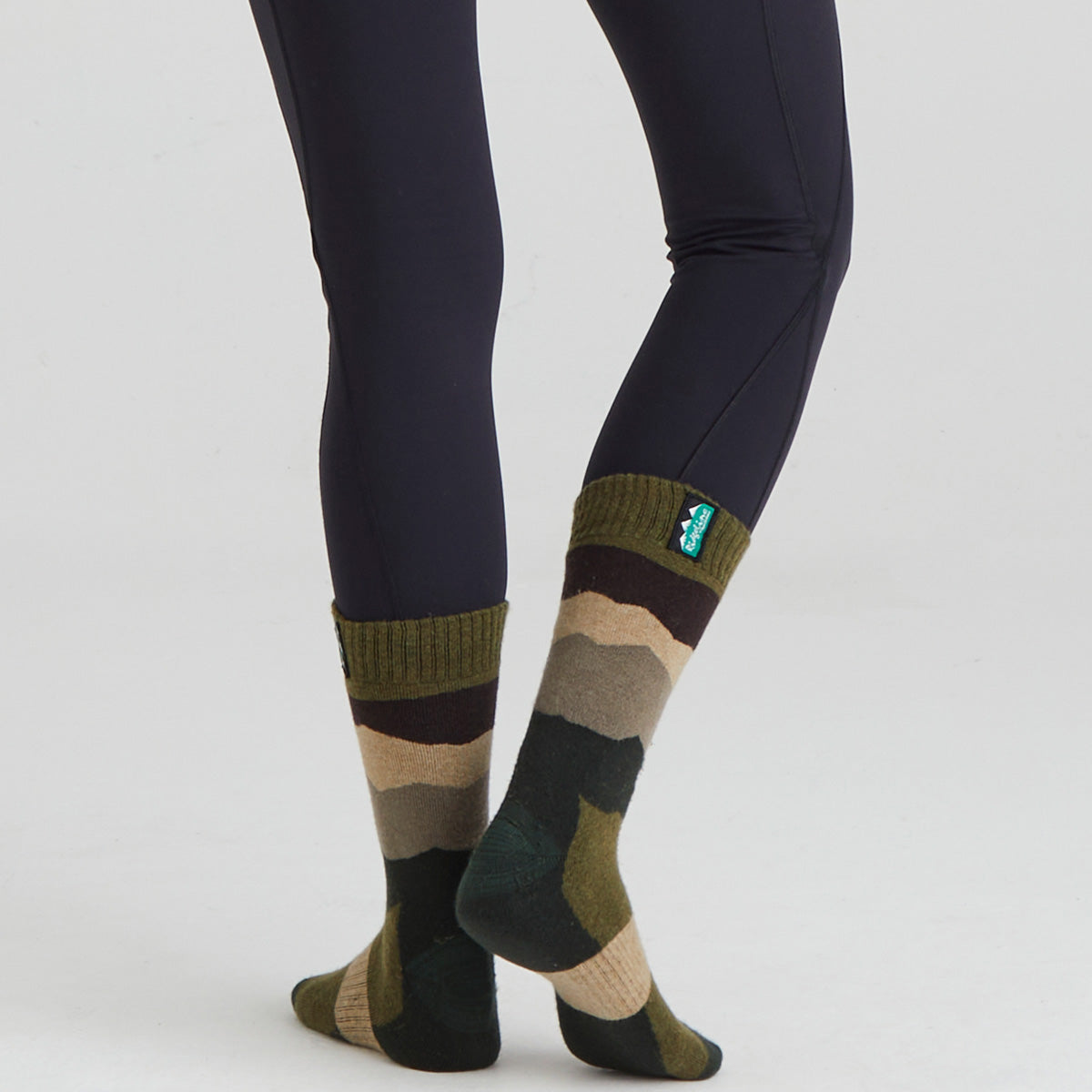 Camouflage-patterned socks worn with dark leggings on a light grey background