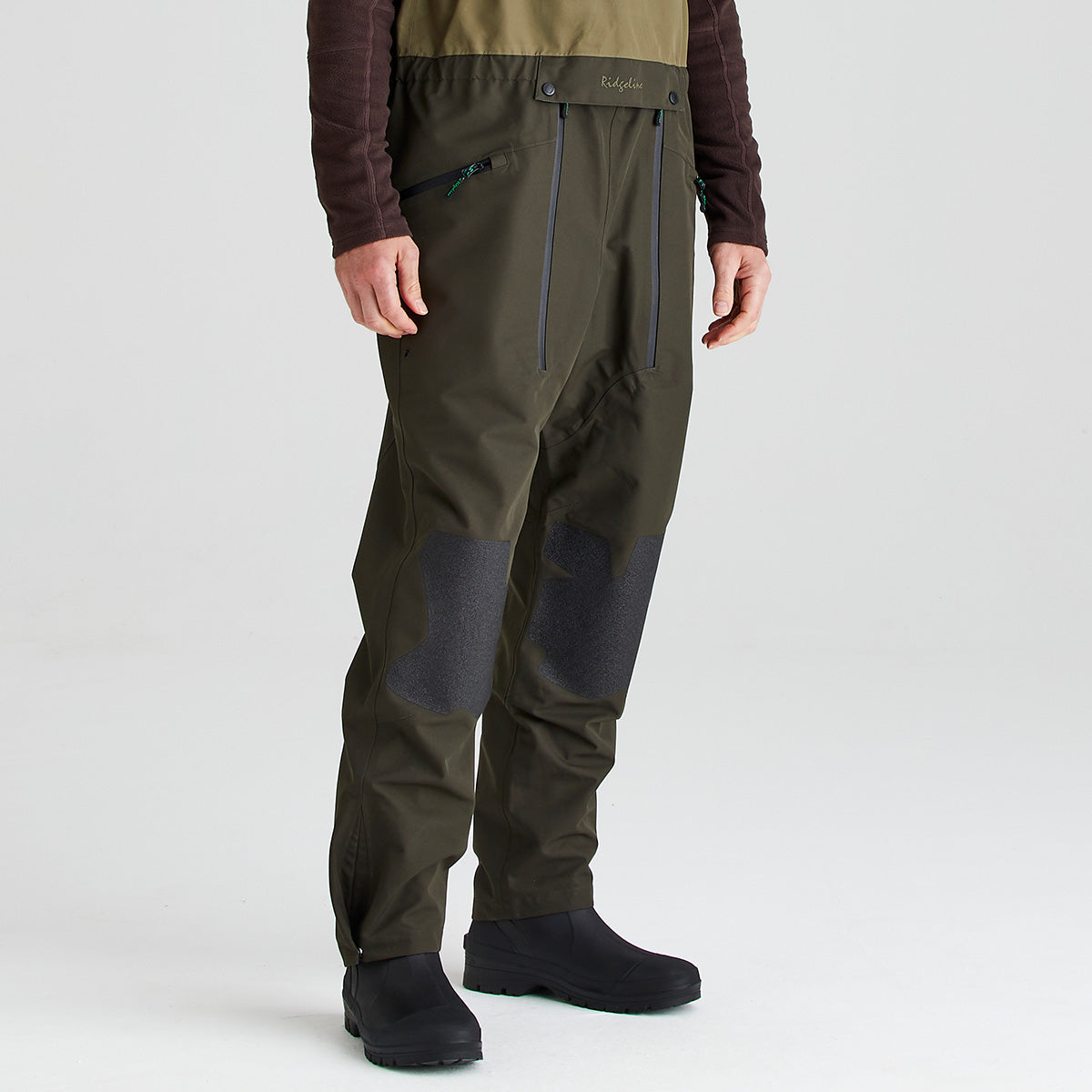 Person wearing green hiking bib & brace on a light gray background