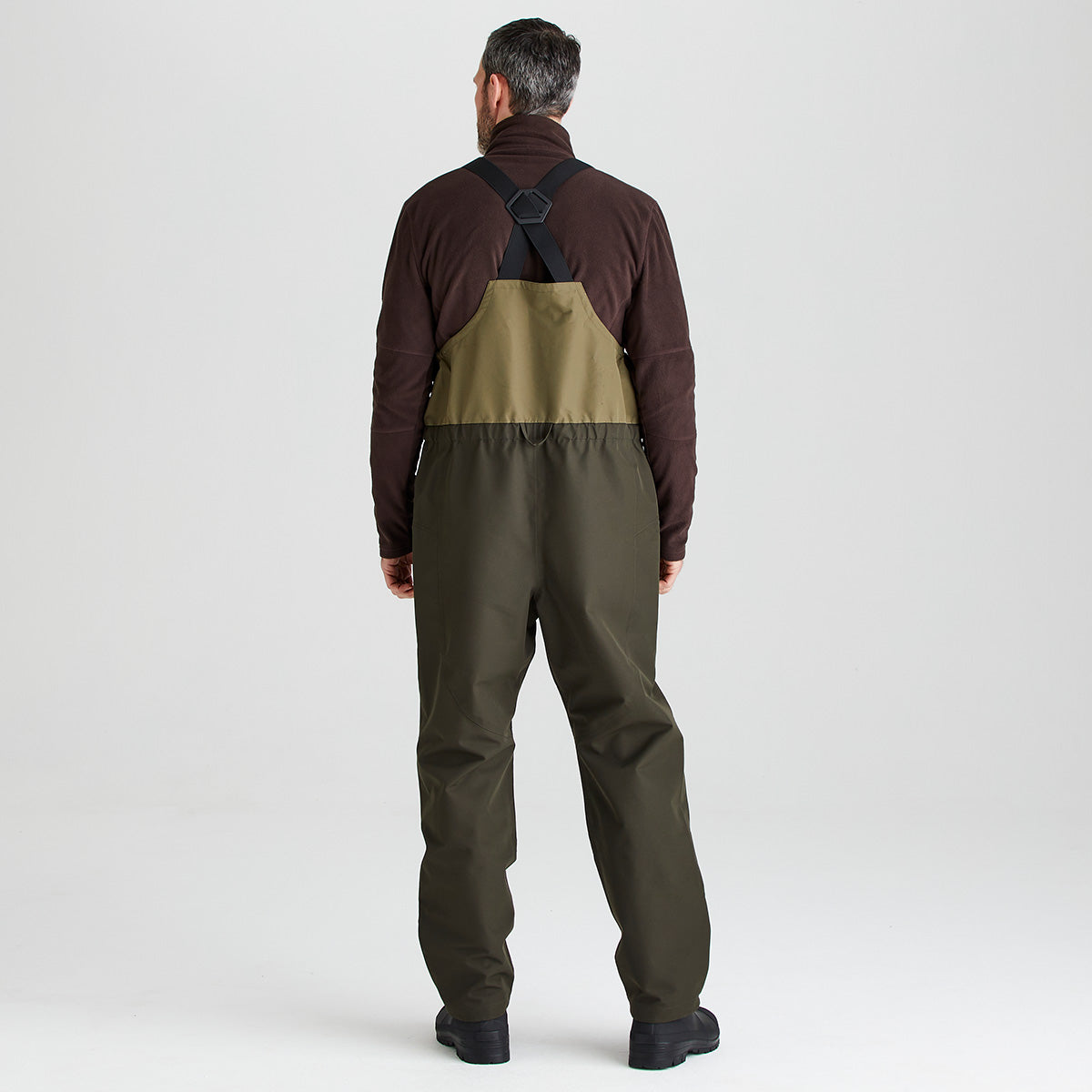 Man wearing a brown fleece and green overalls on a light gray background