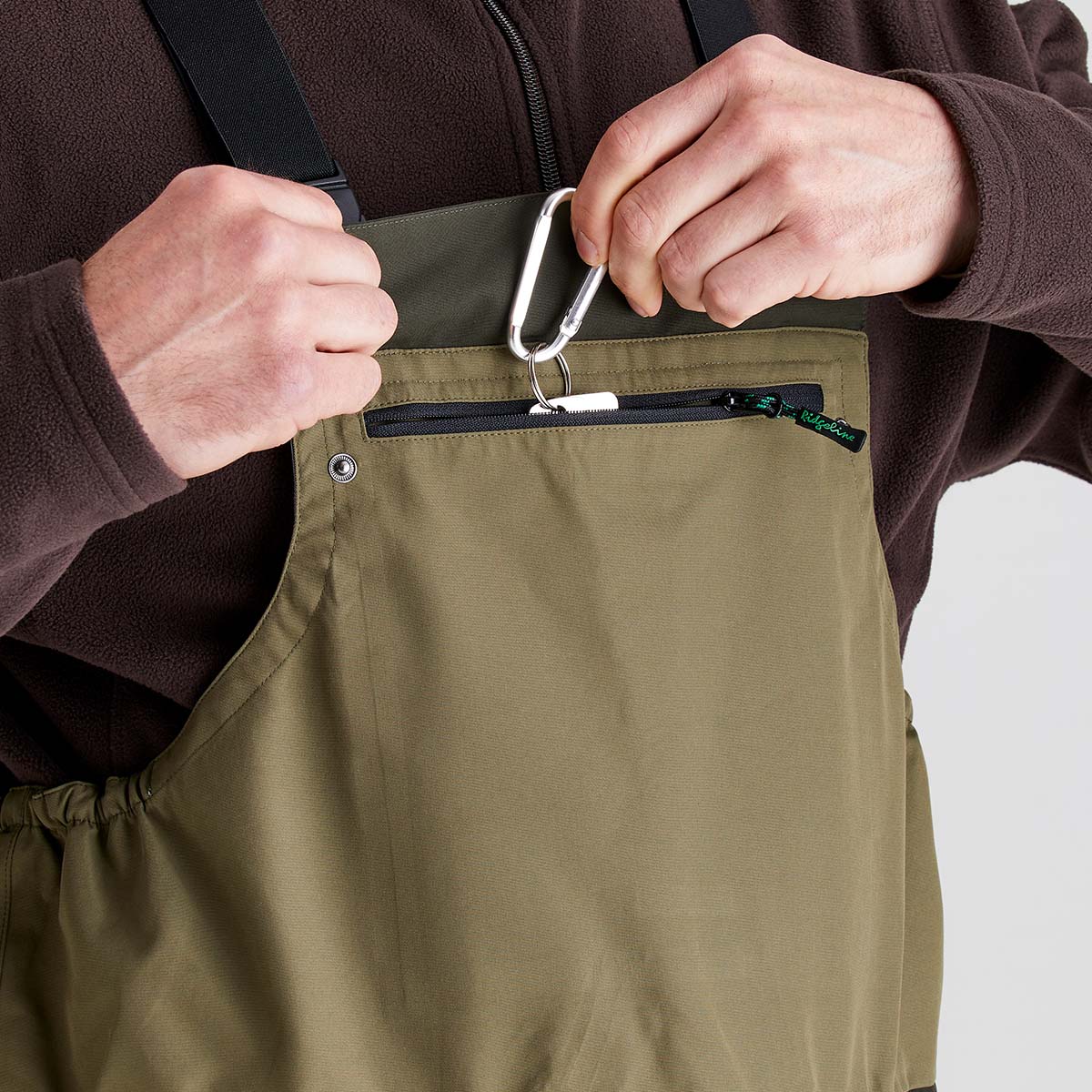 Person wearing a brown fleece with a green overalls, holding keys.