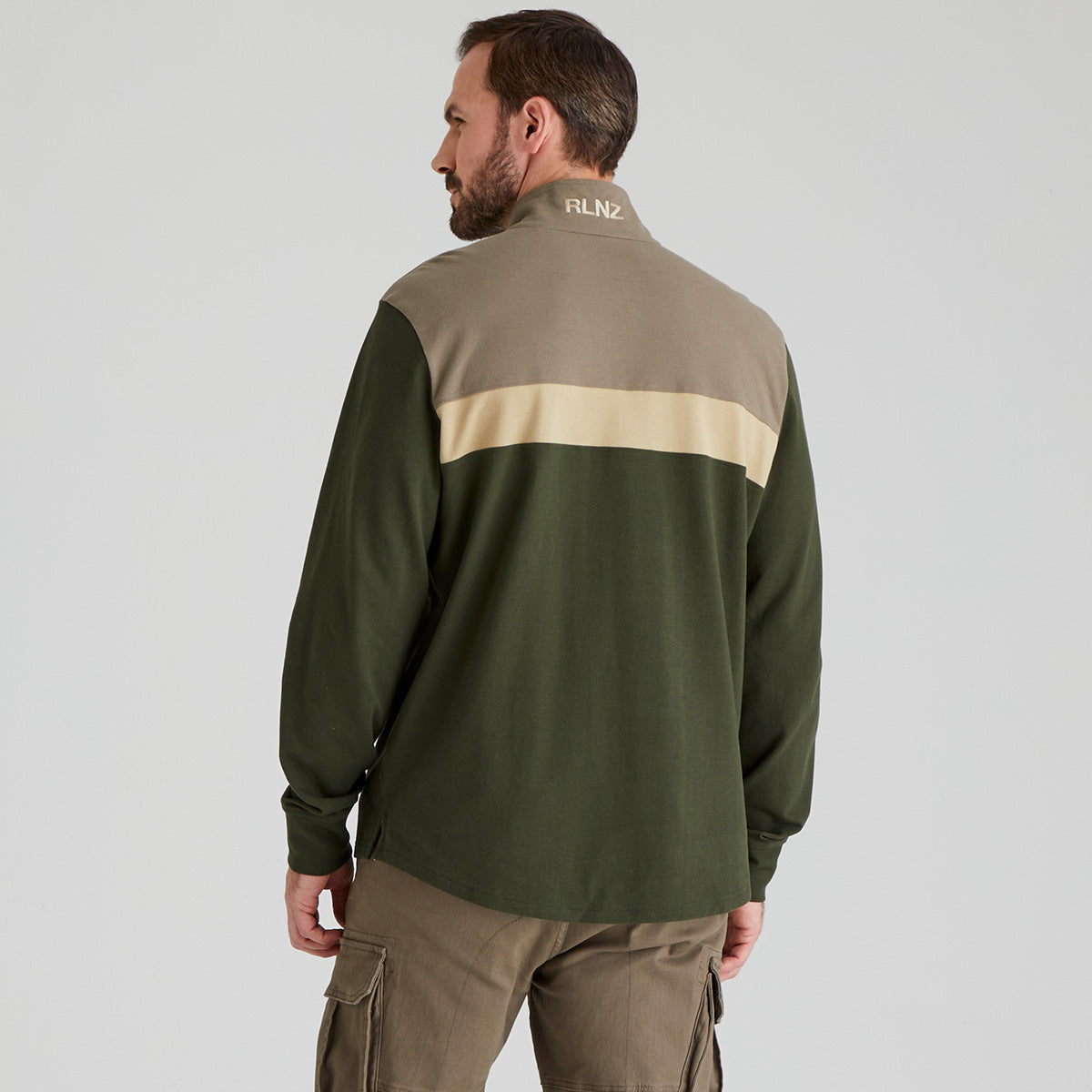 Man wearing a green and beige jacket with 'RLNZ' branding on a grey background