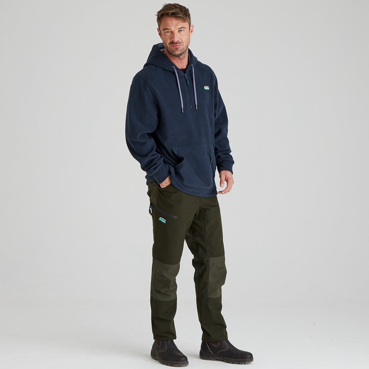 Man wearing a navy fleece hoodie and green pants on a light grey background