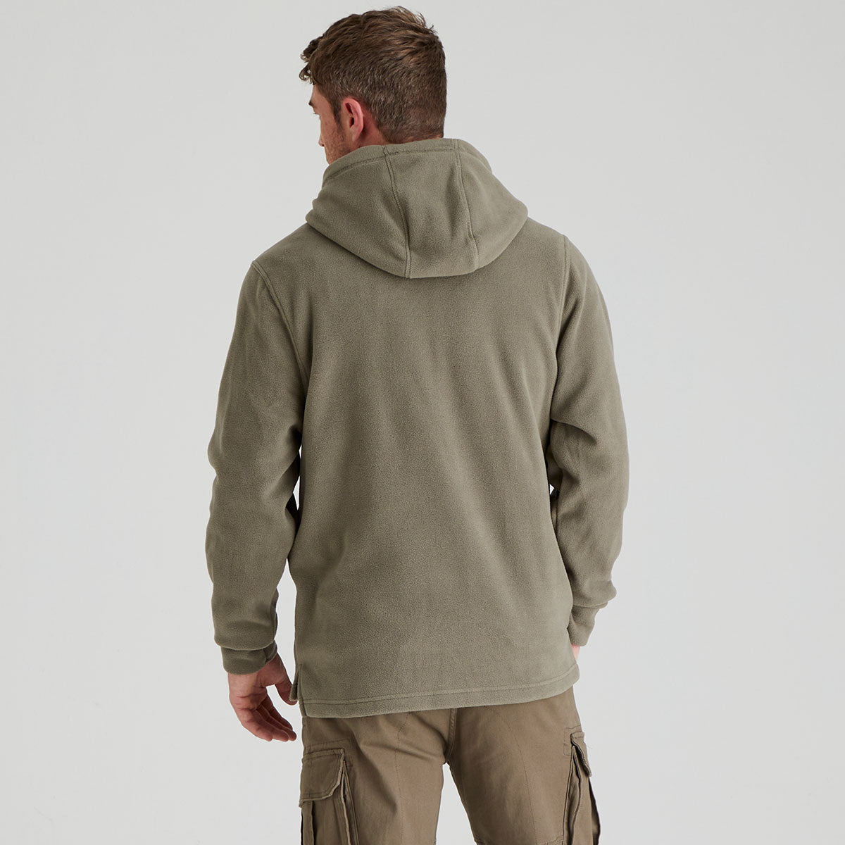 back view of man wearing a green hooded jacket and cargo pants on a light grey background