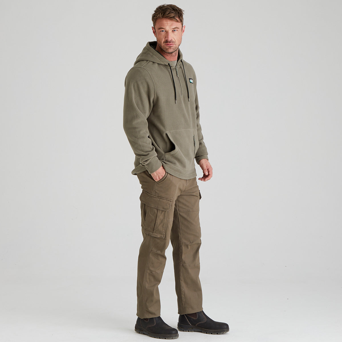 Man wearing a green fleece hoodie and cargo pants on a light grey background