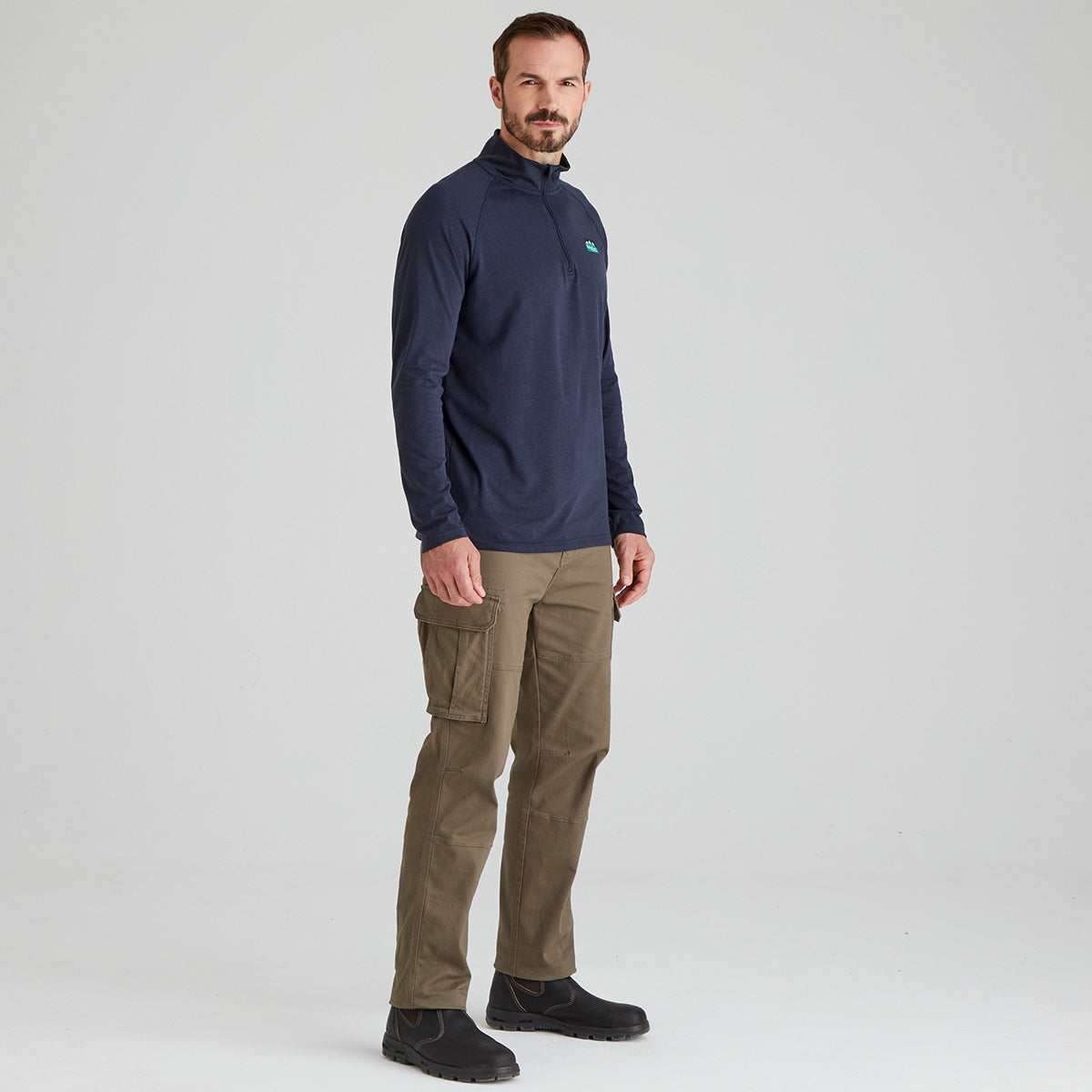 Man wearing a navy pullover and brown pants on a light gray background
