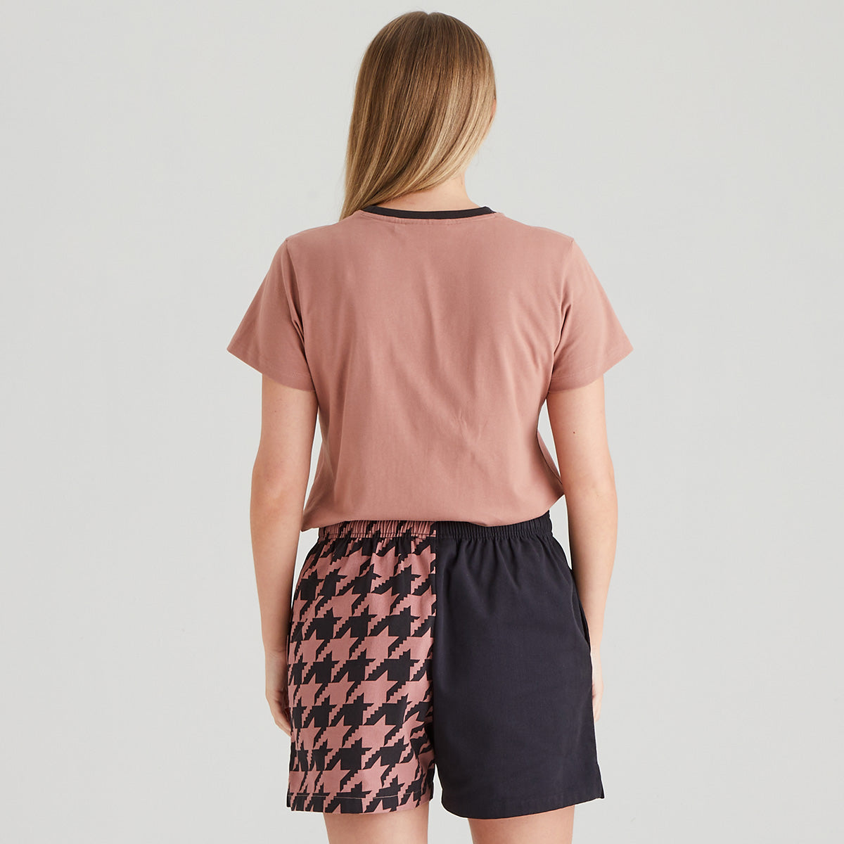 Person wearing a pink t-shirt and patterned shorts on a light gray background