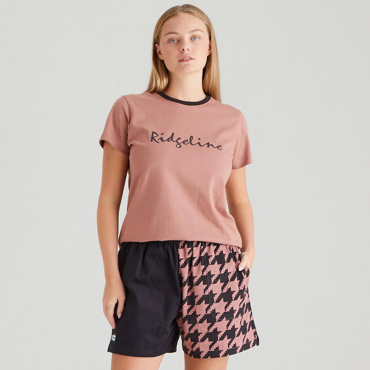 Woman wearing a pink t-shirt with 'Kedeline' branding and patterned shorts on a gray background
