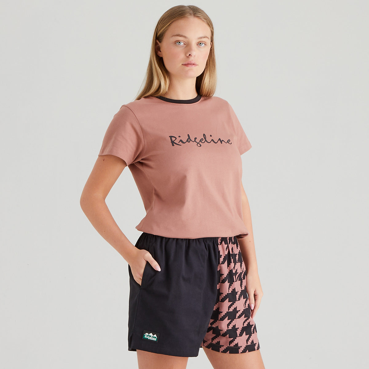 Woman wearing a pink t-shirt with 'Ridgeline' branding and patterned shorts on a plain background