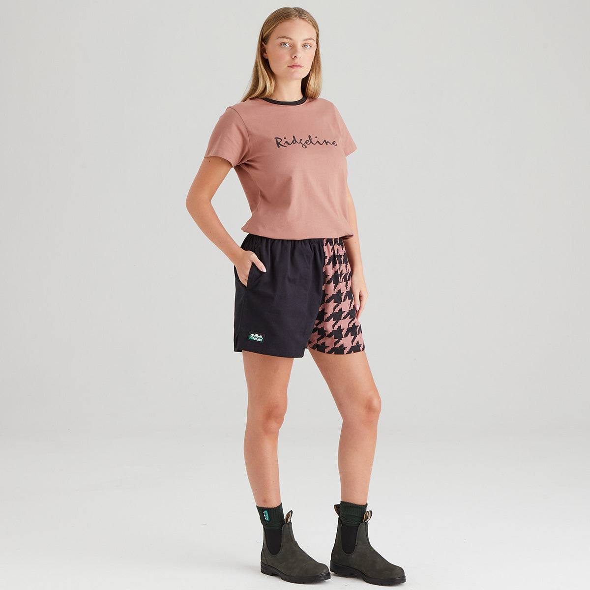 Woman wearing a pink t-shirt and patterned shorts on a plain background