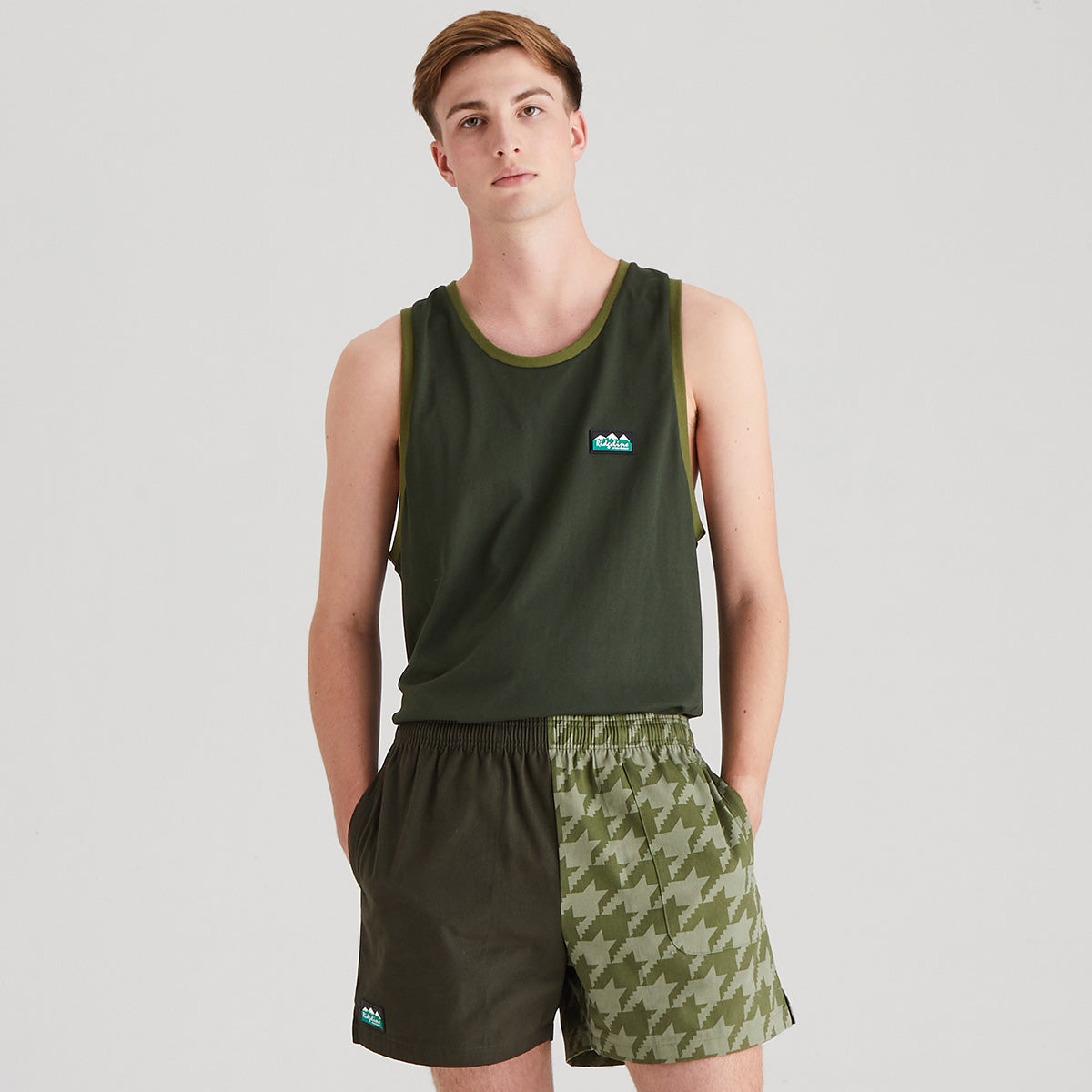 Man wearing a green tank top and shorts with a houndstooth pattern on a white background