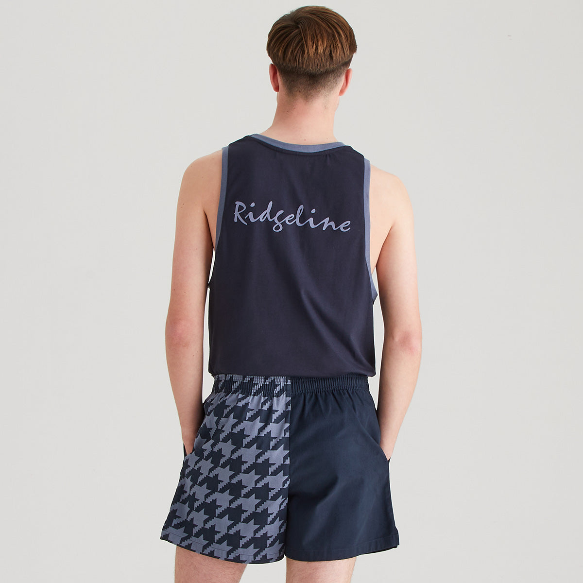 Person wearing a navy tank top with 'Ridgeline' branding and patterned shorts on a light gray background