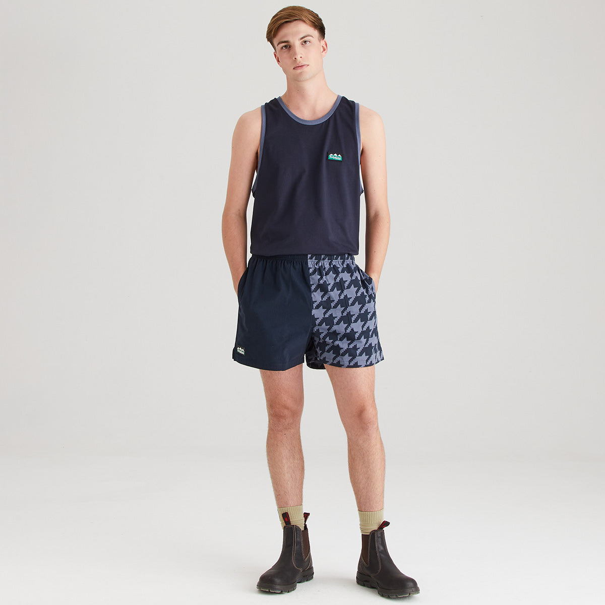 Man wearing a navy tank top and patterned shorts on a white background