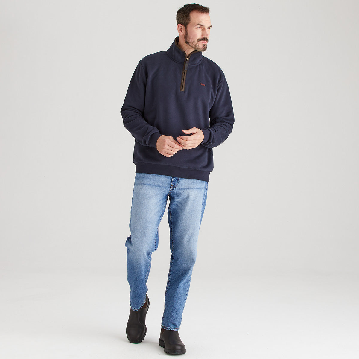 Man wearing a navy pullover and light blue jeans on a gray background