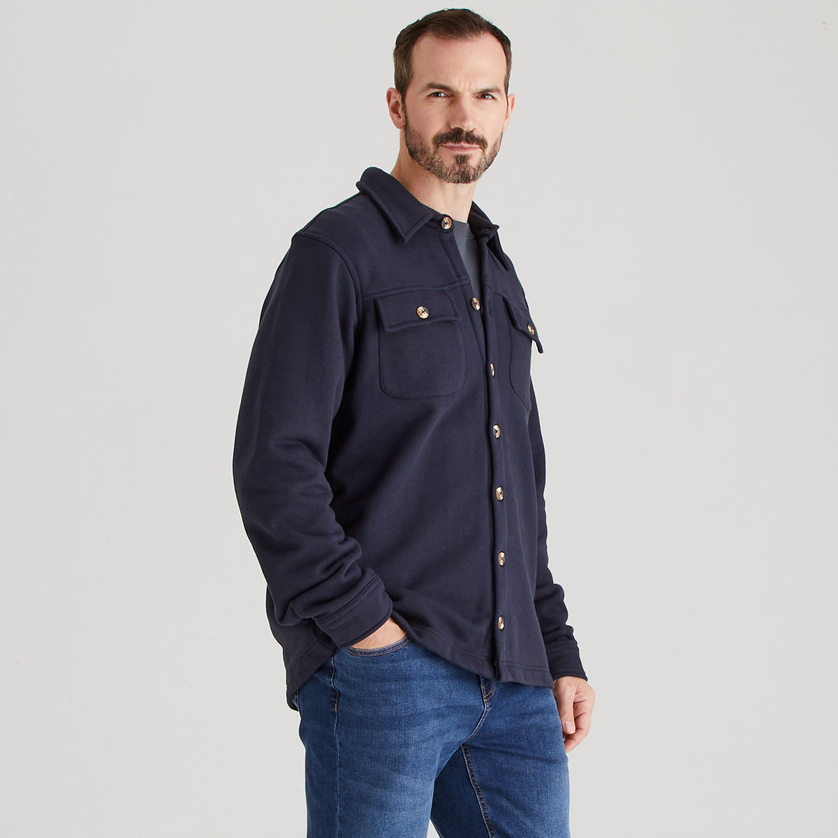 Man wearing a navy blue shirt with gold buttons on a gray background