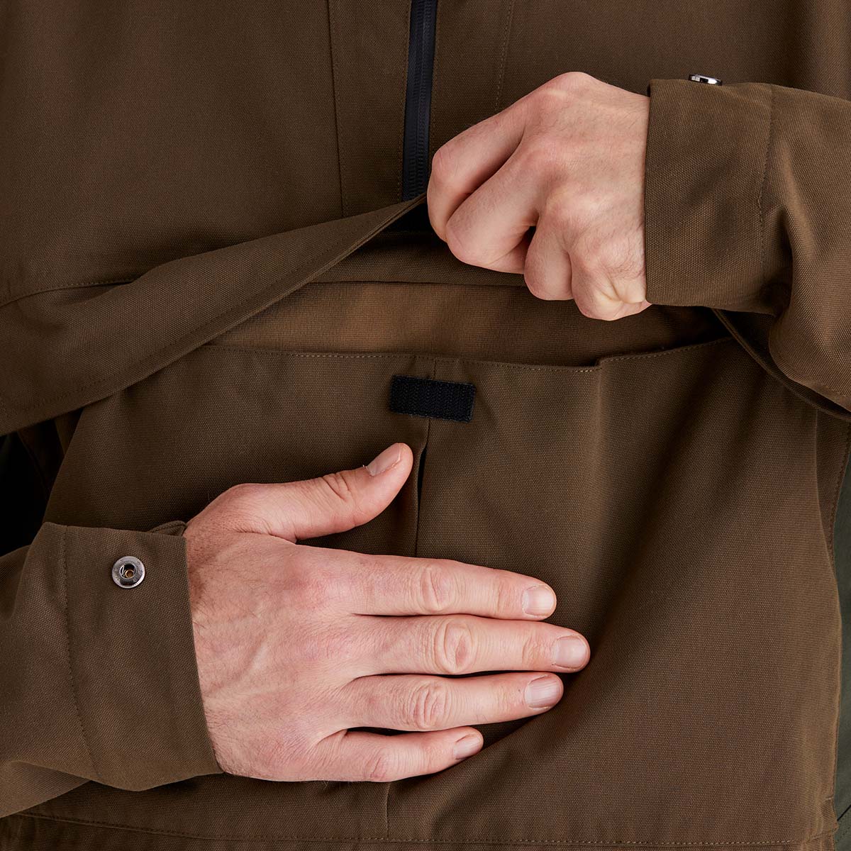Close-up of a person adjusting the chest/ belly pocket of a brown jacket.