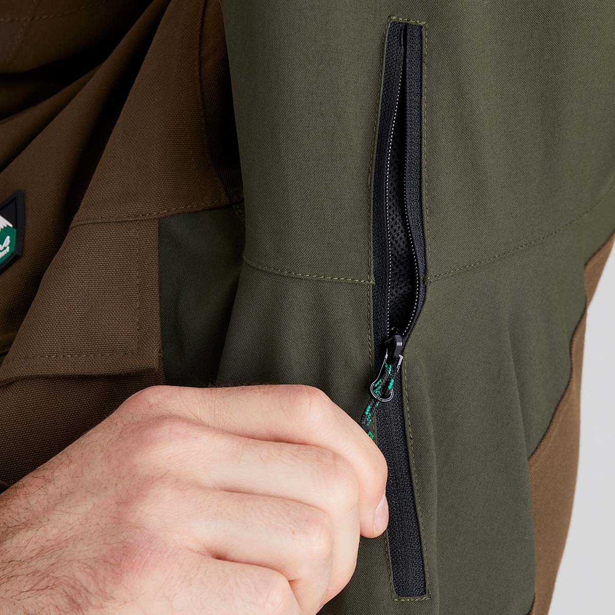 Close-up of a person zipping up a inside zip pocket with a brand logo on the sleeve.