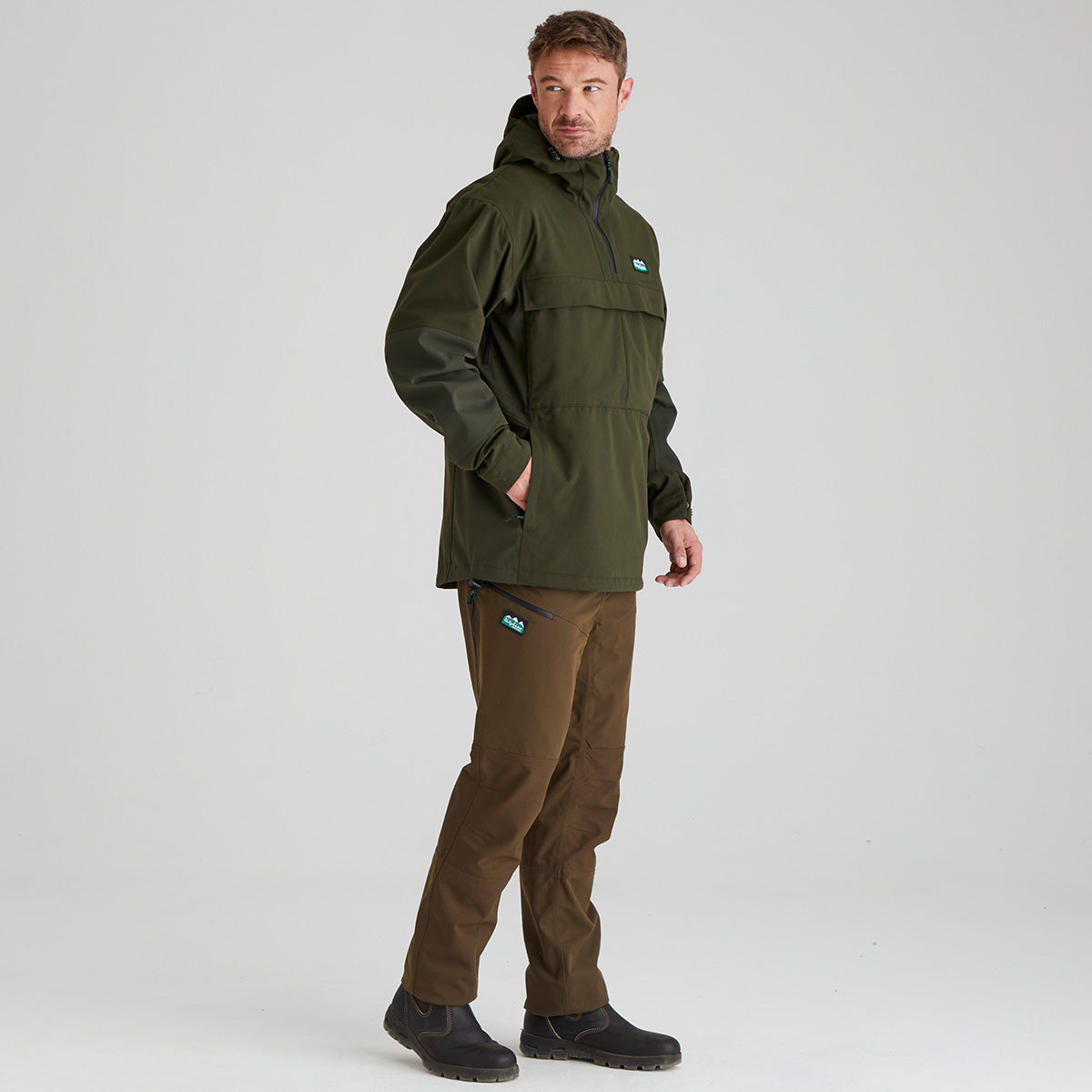 Olive green hooded overhead smock with half zip front and chest pocket, side view with hand in pocket