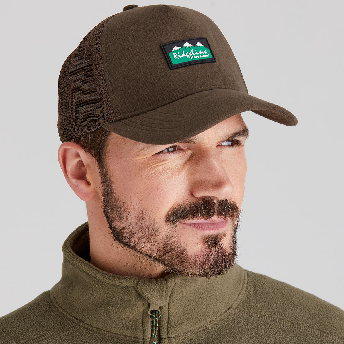 Man wearing a brown cap with a logo on a gray background