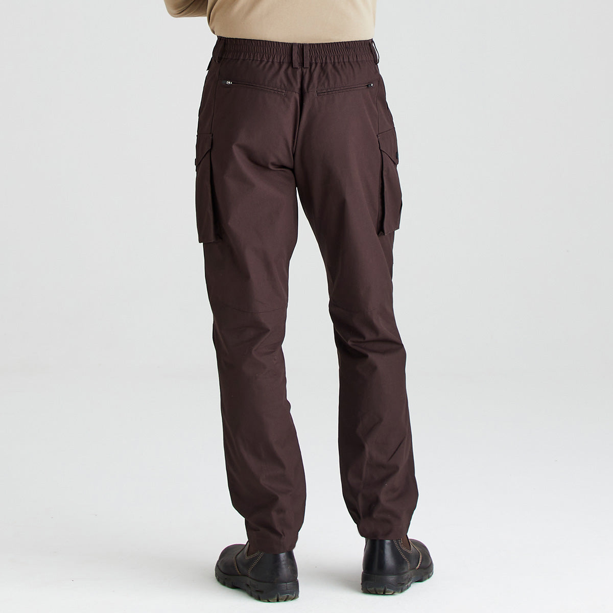 A person shown from the back wearing dark brown cargo pants with an elastic waistband, side cargo pockets, and black shoes against a light gray studio background.
