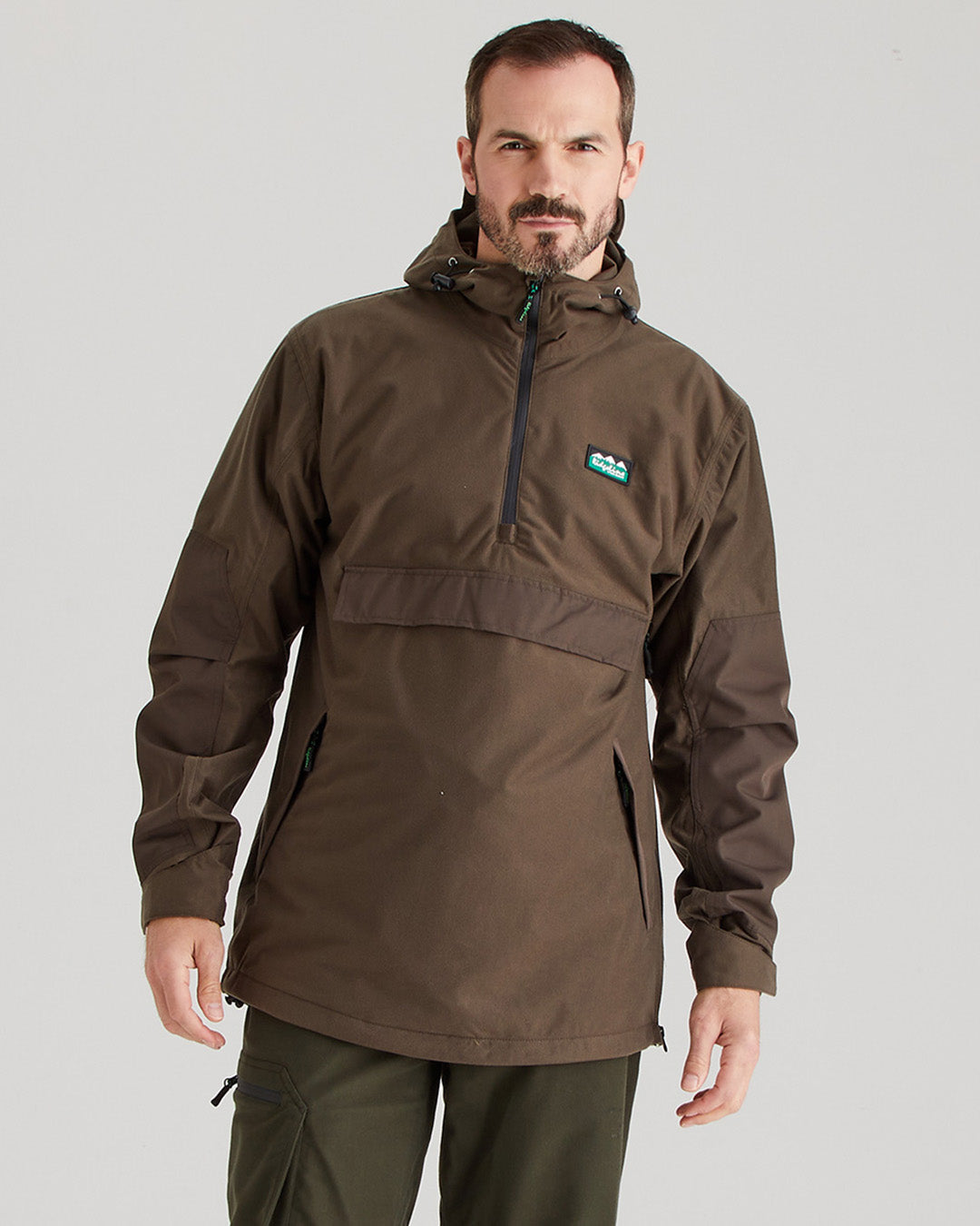 Man wearing a brown jacket with a brand logo on a gray background